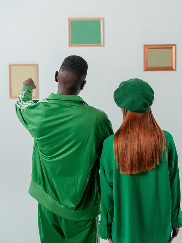 Two people wearing green look at framed images on a wall