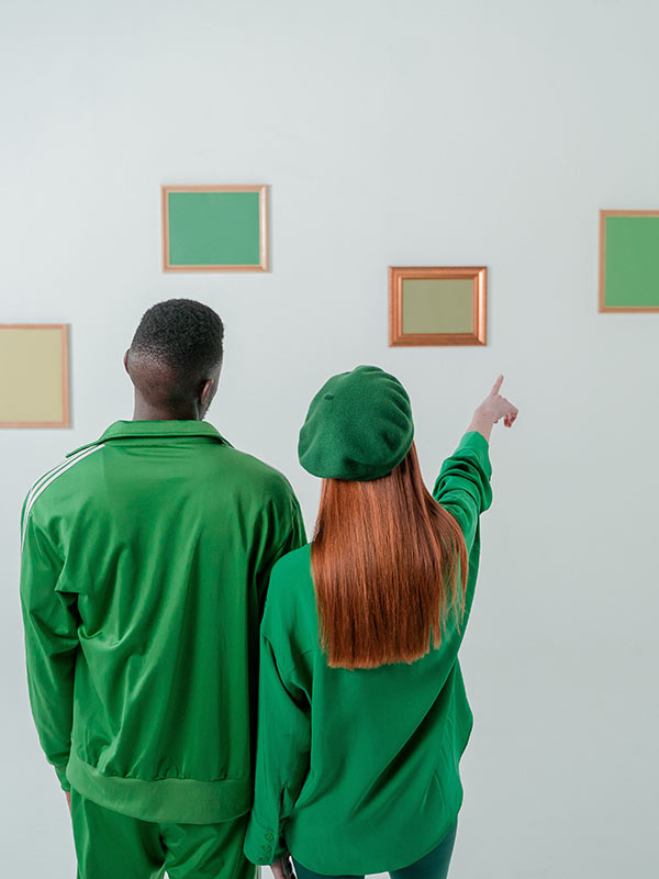 Two people wearing green discuss framed images on a wall.