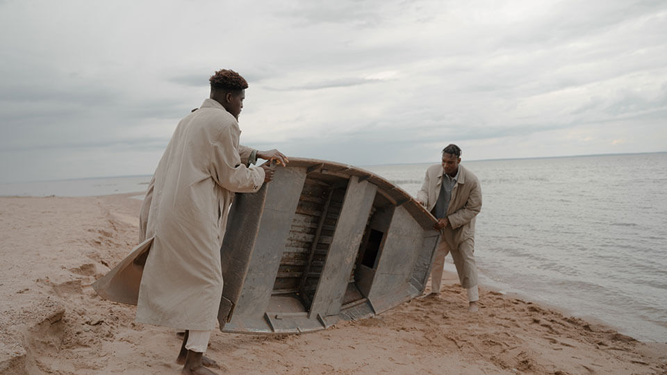 Two men holding boat in sand at beach.