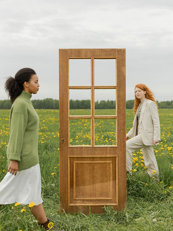 Two women walking around door in open field.