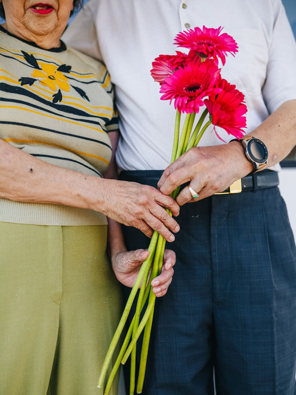 Old couple holding flowers in their hands.