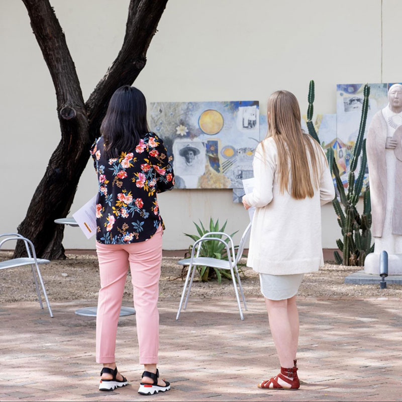 Two women admiring a painting  in an outdoor gallery