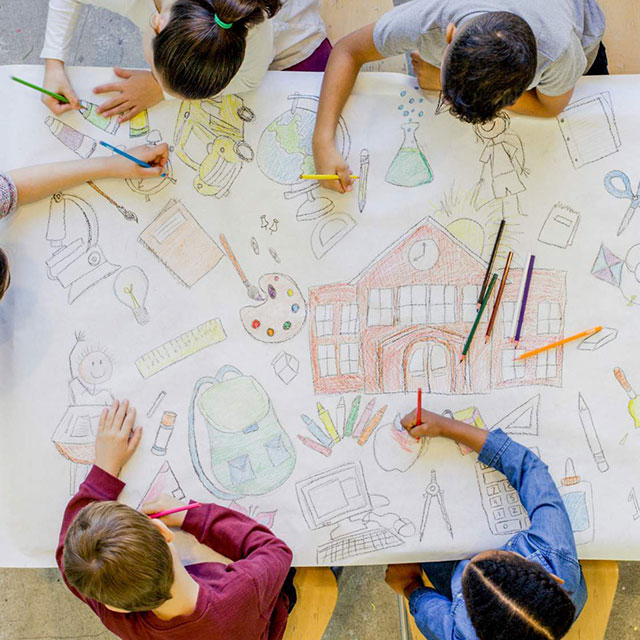 Overhead view of children drawing on a large piece of paper