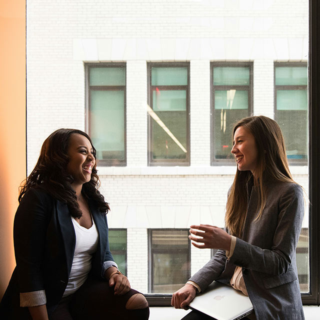 Two women sitting in a window sill talking